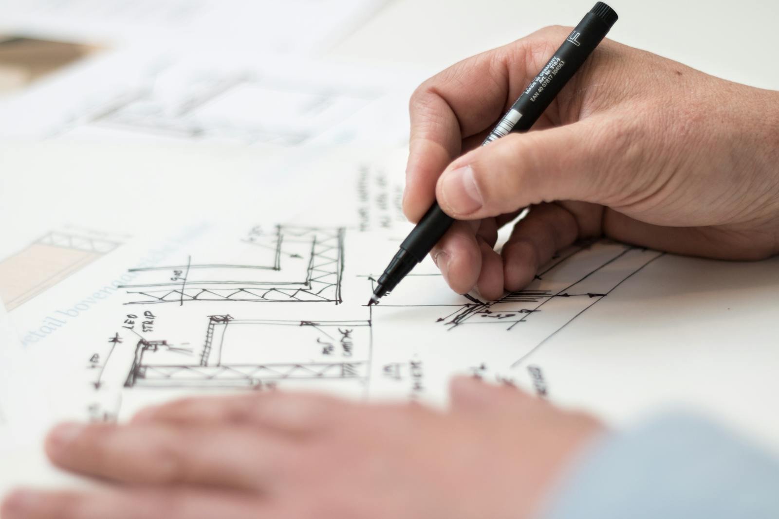 Equipo VGH Arquitectura Horcajuelo Close-up of hand drawing intricate technical designs on blueprint with pen, ideal for engineering or architecture themes.